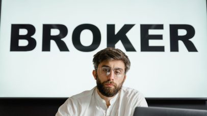 Portrait of a confident businessman sitting in an office under the sign 'BROKER'.