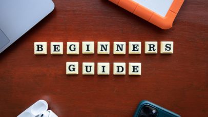 Creative flat lay of gadgets and 'Beginners Guide' text on wooden table.